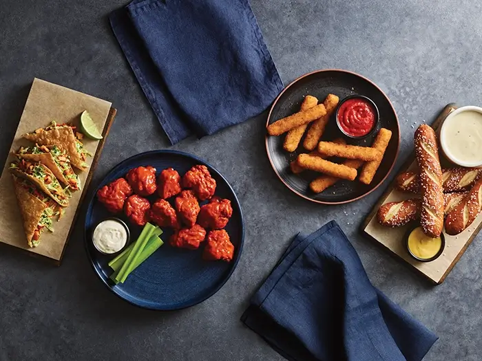 Appetizer spread with boneless wings, tacos, mozzarella sticks and soft pretzels with dipping sauces.