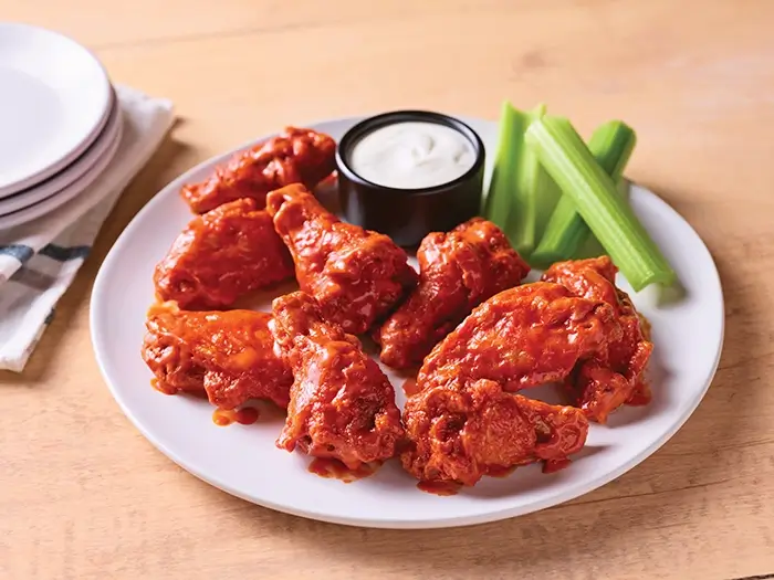 Buffalo wings served with celery sticks and ranch dipping sauce on a white plate.